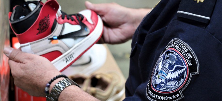 A CBP agent holds one of more than 14,800 pair of counterfeit Nike shoes, seized in a shipment arriving from China at the Los Angeles-Long Beach sports complex in 2019. 