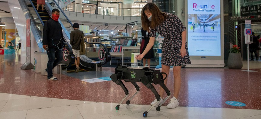A woman disinfects her hands from a mobile robot that carries a container of sanitization liquid at Central World, an upmarket shopping mall in Bangkok, Thailand in May 2020.