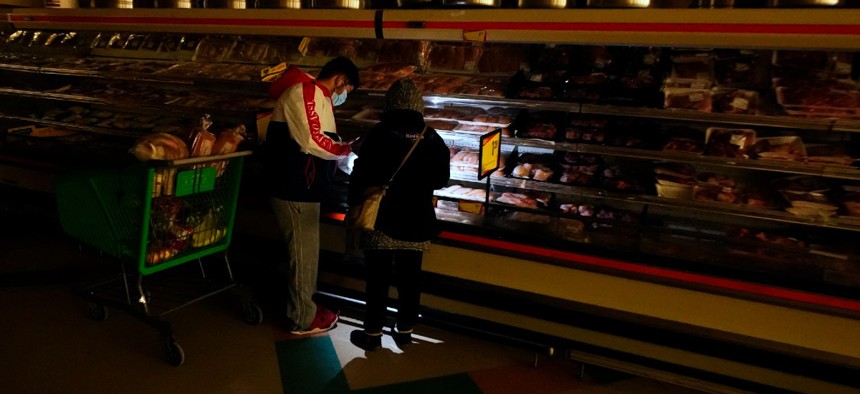 Customers use the light from a cell phone to look in the meat section of a grocery store Tuesday, Feb. 16, 2021, in Dallas. Even though the store lost power, it was open for cash only sales.