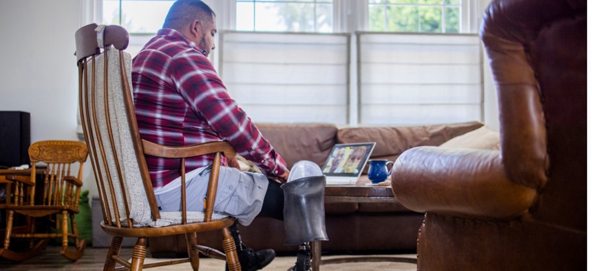 A Hispanic American veteran double amputee on a telemedicine call with his doctors at home.