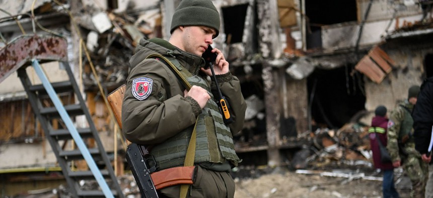 A Ukrainian serviceman talks on a smartphone in front of a damaged residential building at Koshytsa Street, a suburb of the Ukrainian capital Kyiv, where a military shell allegedly hit, on February 25, 2022.