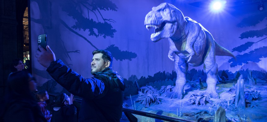 Man takes a selfie on his smartphone with the animatronic Tyrannosaurus at the dinosaurs exhibition room at the Natural History Museum on 27th April 2022 in London, United Kingdom. The T. rex is a genus of coelurosaurian theropod dinosaur. The museum exhibits a vast range of specimens from various segments of natural history. The museum is home to life and earth science specimens comprising some 80 million items within five main collections: botany, entomology, mineralogy, paleontology and zoology. The museum is a centre of research specialising in taxonomy, identification and conservation