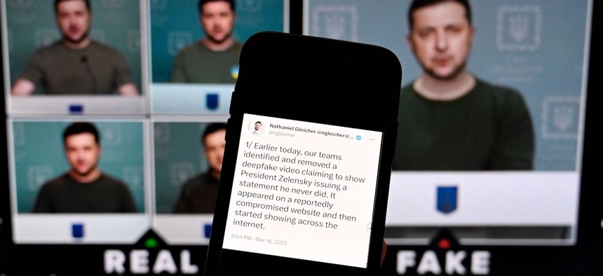 This illustration photo taken on January 30, 2023 shows a phone screen displaying a statement from the head of security policy at META with a fake video (R) of Ukrainian President Volodymyr Zelensky calling on his soldiers to lay down their weapons shown in the background.