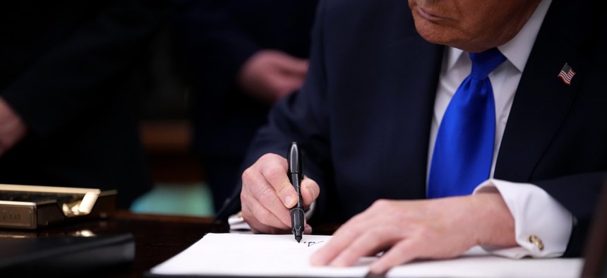 Trump signing an executive order on April 30, 2026. Schedule F was first proposed via executive order in October 2020 and was rescinded during the Biden administration. 