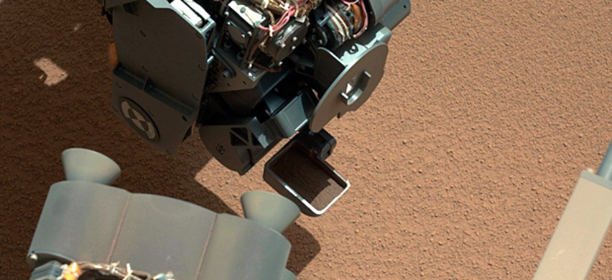 The Curiosity Rover uses it's robotic arm to scoop sand.
