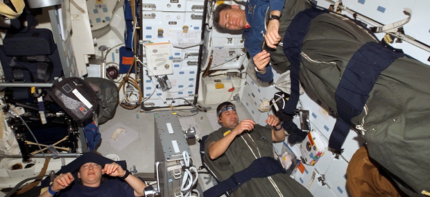 Astronauts Pam Melroy, George Zamka, bottom right,and European Space Agency's Paolo Nespoli, sleep in their sleeping bags, which are secured on the middeck of the Space Shuttle Discovery while docked with the International Space Station.