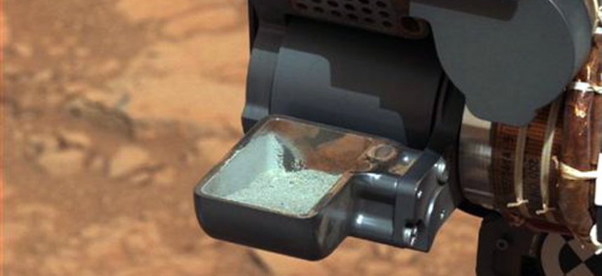 The Curiosity rover holding a scoop of powdered rock on Mars. The rover recently drilled into a Martian rock for the first time and transferred a pinch of powder to its instruments to analyze the chemical makeup.