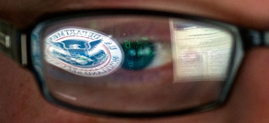 A reflection of the Department of Homeland Security logo is seen reflected in the glasses of a cyber security analyst.