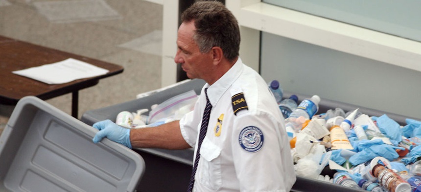 A TSA worker empties bottles into a bin filled with confiscated items at Denver International Airport.