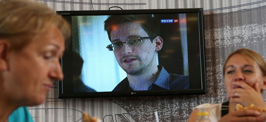 Two Russians eat lunch at Moscow's Sheremetyevo airport while a report about Edward Snowden plays on a nearby TV.
