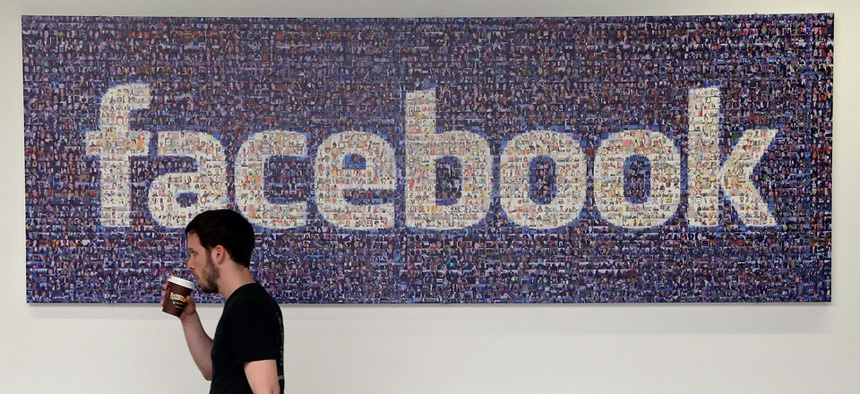 A Facebook employee walks past a sign at Facebook headquarters in Menlo Park, Calif.