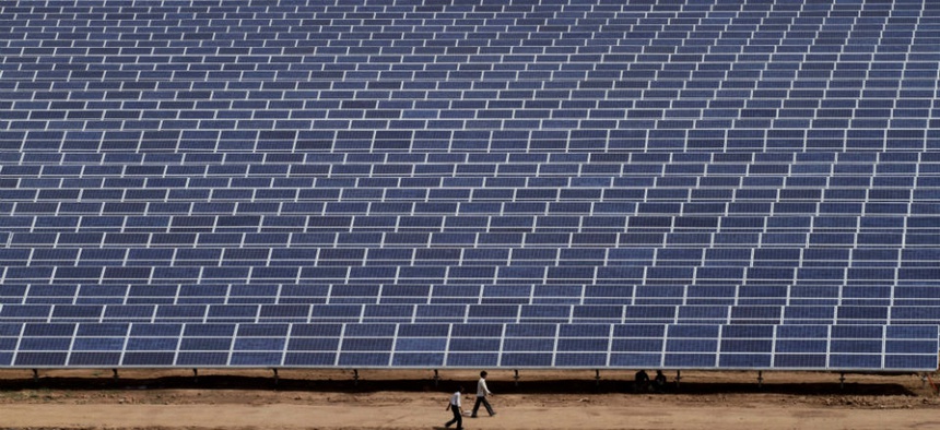 Indian workers walk past solar panels at the 200 megawatt Gujarat Solar Park.