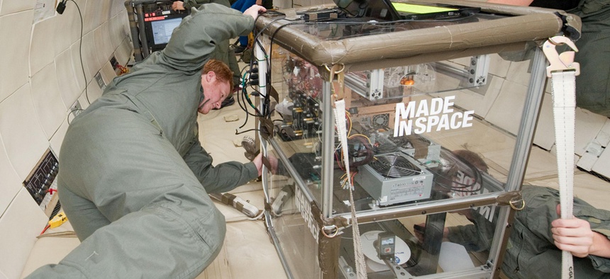 Two people monitoring the performance of extruders inside the Made In Space experiment box during a microgravity portion of flight aboard a modified Boeing 727 from the Zero G Corporation.