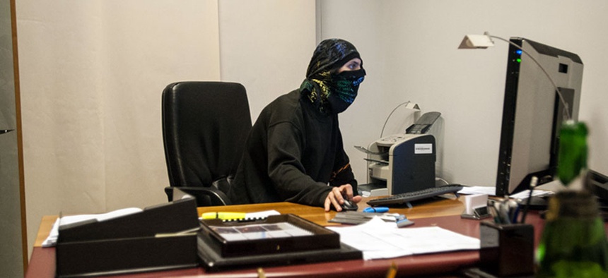 A masked pro-Russian activist sits in front of a computer inside a room.