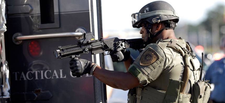 A member of the St. Louis County Police Department points his weapon in the direction of a group of protesters in Ferguson, Mo.