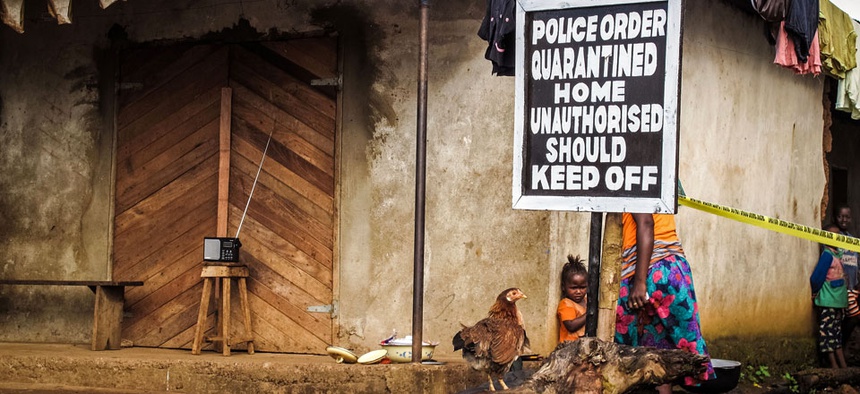 A child, center, stands underneath a signboard reading 'Police order quarantined home unauthorised should keep off' as a family home is placed under quarantine due to the Ebola virus in Port Loko, Sierra Leone.