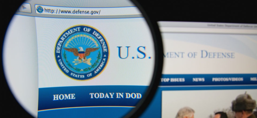 Photo of the United States Department of Defense homepage on a monitor screen through a magnifying glass.
