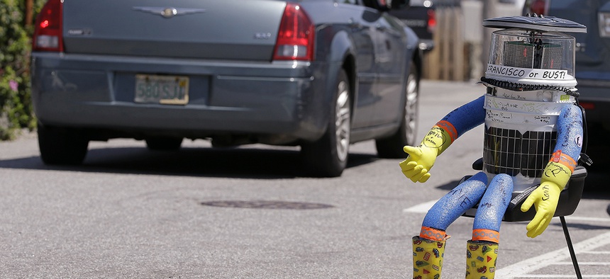 A car drives by HitchBOT, a hitchhiking robot in Marblehead, Mass.