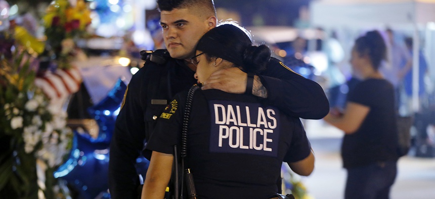 Dallas police officers comfort each other Friday, July 8, 2016, in Dallas in front of police cars decorated as a public memorial in front of police headquarters, in honor of Dallas police who were killed Thursday.