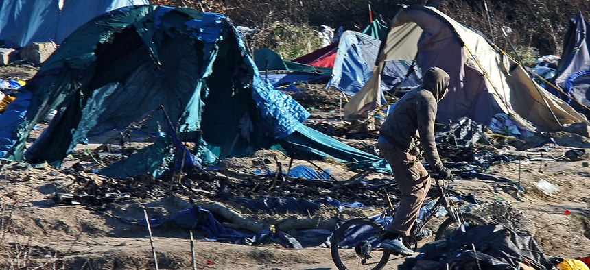A migrant rides with his bicycle in the Calais refugee camp, northern France Tuesday, Jan. 19, 2016.