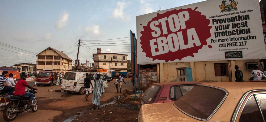 People pass a banner reading 'STOP EBOLA' forming part of Sierra Leone's Ebola free campaign in the city of Freetown, Sierra Leone, Friday, Jan. 15, 2016.