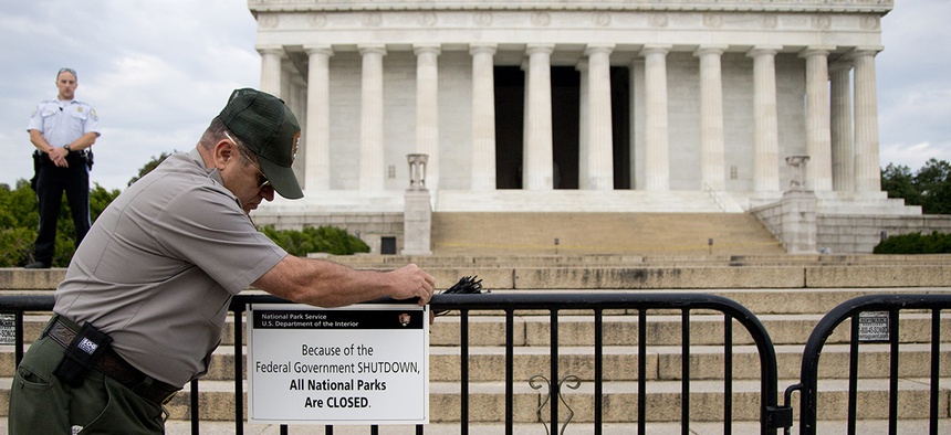 A U.S. Park Police officer watches at left as a National Park Service employee posts a sign on a barricade closing access to the Lincoln Memorial in Washington.