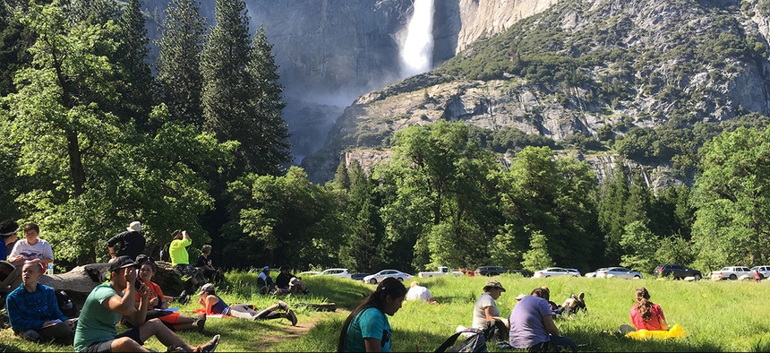 Visitors sit in a meadow at Yosemite National Park, Calif., below Yosemite Falls.