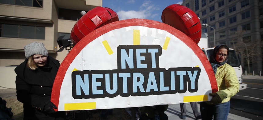 Protesters carry the top of an alarm clock display that reads "Net Neutrality" after a protest at the FCC headquarters in Washington.