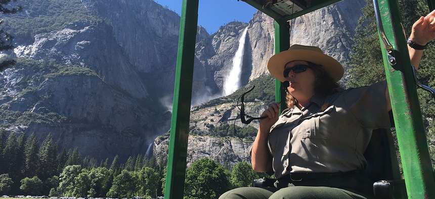 A guide at Yosemite National Park, Calif., talks to tourists with Yosemite Falls behind her.