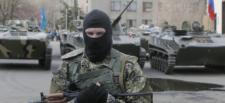 A masked gunman guards combat vehicles with Russian, Donetsk Republic and Ukrainian paratroopers, flags and gunmen on top, parked in downtown of Slovyansk.