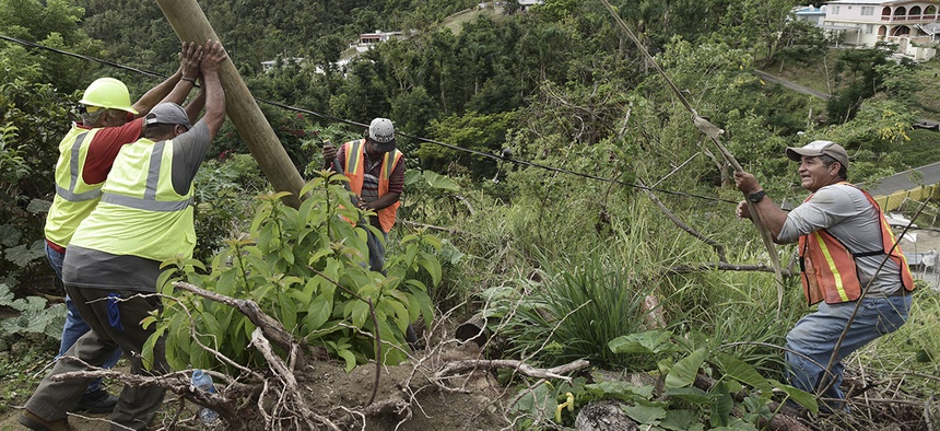 Public Works Sub-Director Ramon Mendez, wearing a hard hat at left, works with locals who are municipal workers, from right, Eliezer Nazario, Tomas Martinez and Angel Diaz as they install a new post to return electricity in Coamo, Puerto Rico.