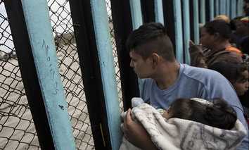 A member of the Central American migrant caravan, holding a child, looks through the border wall toward a group of people gathered on the U.S. side, as he stands on the beach where the border wall ends in the ocean, in Tijuana, Mexico, April 29, 2018.