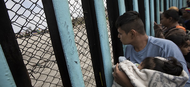 A member of the Central American migrant caravan, holding a child, looks through the border wall toward a group of people gathered on the U.S. side, as he stands on the beach where the border wall ends in the ocean, in Tijuana, Mexico, April 29, 2018.
