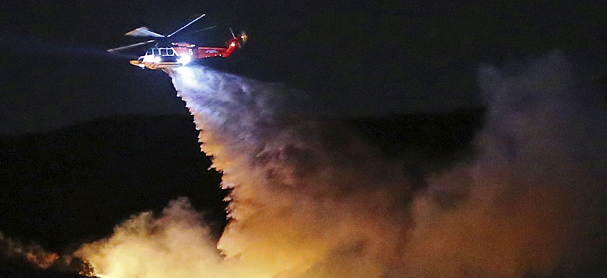 a helicopter drops water on a brush fire that broke out in Topanga State Park, Los Angeles.