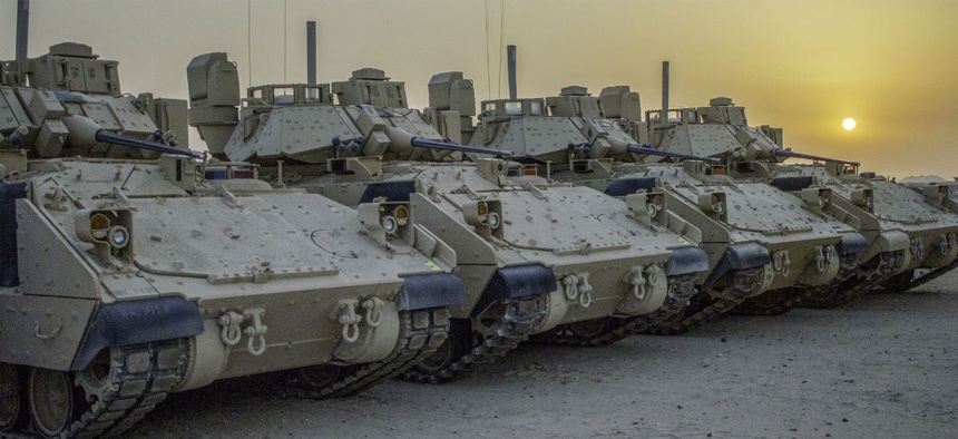 Four M2A3 Bradley Infantry Fighting Vehicles are illuminated by the rising sun in a motor pool located at Camp Buehring, Kuwait, July 19, 2018.