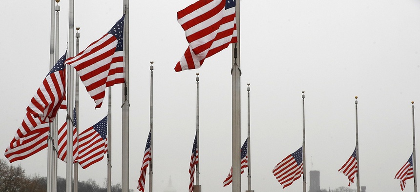 With a misty U.S. Capitol in the distance, the American flags surrounding the Washington Monument fly at half-staff, Saturday, Dec. 1, 2018, in Washington.